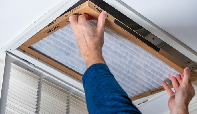 A person replacing an air filter in a ceiling vent.